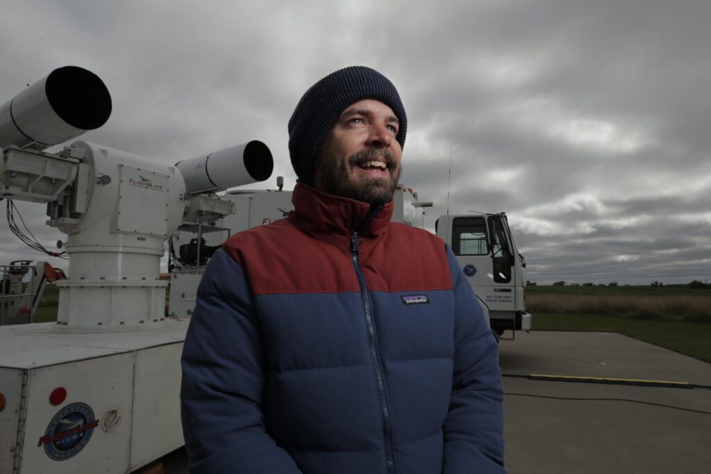 A smiling person outdoors under a cloudy sky, wrapped up in warm jacket and woolly hat.