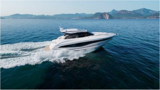 Motor yacht speeding along through the sea with rocky hills in the background.