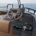 Cockpit of motorboat showing steering wheel, throttle and mobile phone charging pod, with views ahead of the sea and horizon.