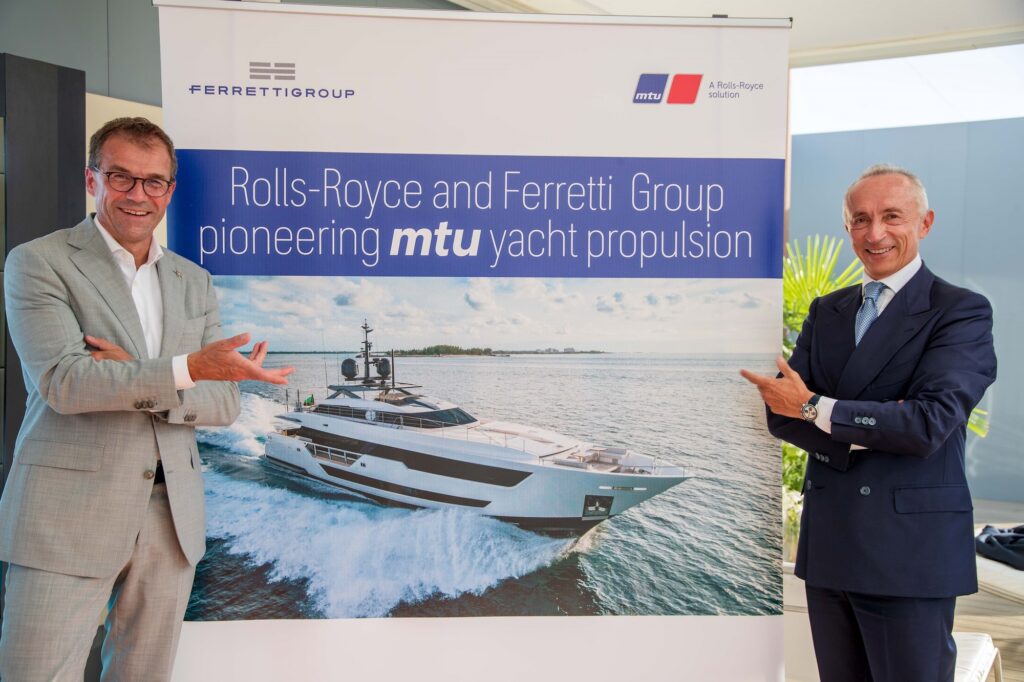 Deux hommes debout de part et d'autre d'une affiche représentant un yacht, qui annonce l'accord des entreprises.