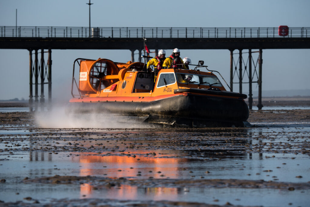 Orange and black RNLI rescue hovercraft skimming over the surface of the sand