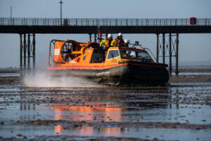 Orange and black RNLI rescue hovercraft skimming over the surface of the sand