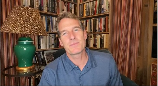 Historian Dan Snow in a room with book lined walls with a green based lamp
