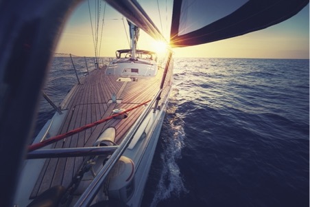 Picture taken from bow of yacht down its length, sailing in the middle of the ocean at sunset.