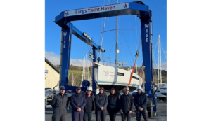 Line-up of people standing in front of a boat that is in a hoist at a marina.