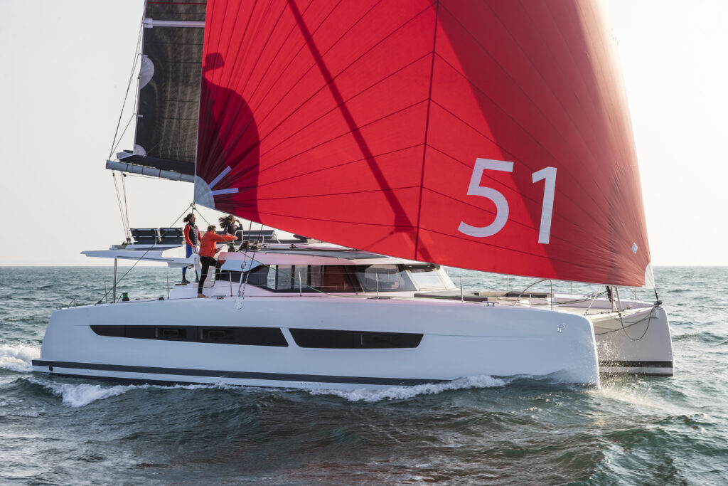 Catamaran sailing with a large red headsail with 51 one it