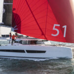 Catamaran sailing with a large red headsail with 51 one it