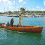 wooden steam boat with two people onboard and a red ensign flying