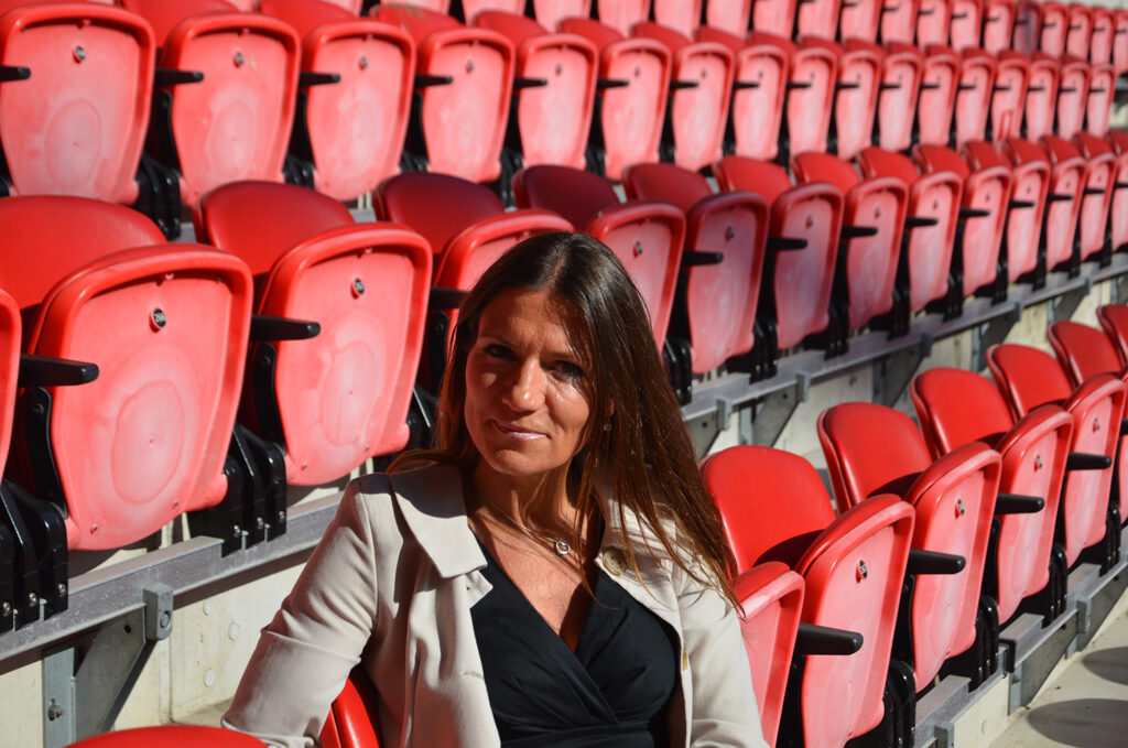 Polly Handford sentada en asientos rojos en el estadio de fútbol