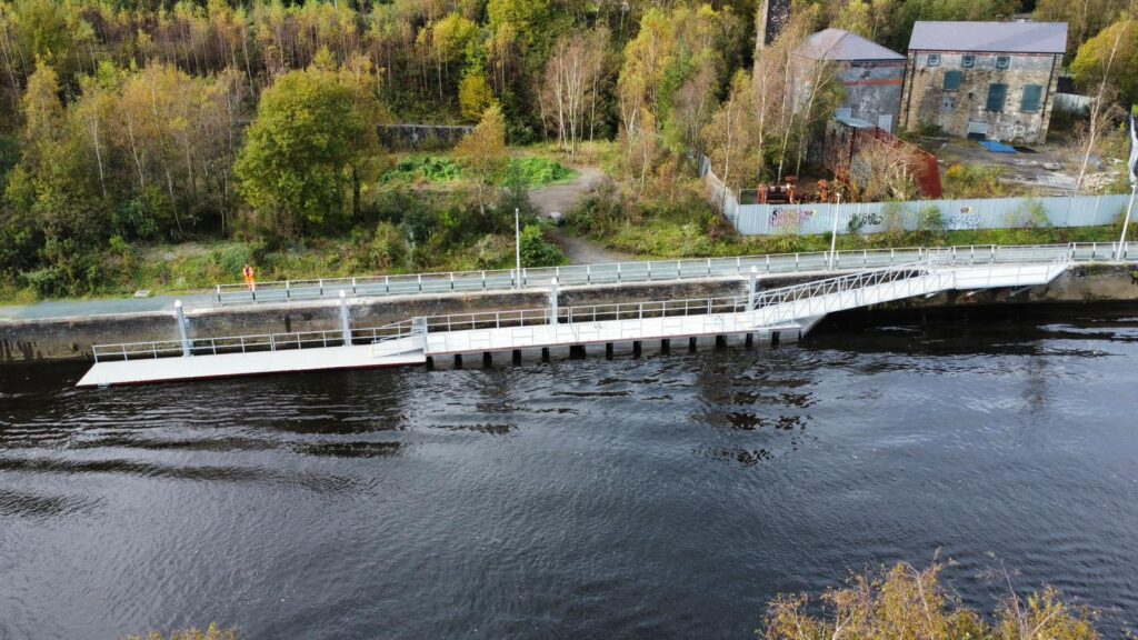 bridge pontoon along bank of river with greenery in the background