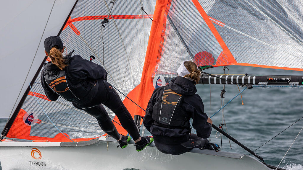 two young dinghy sailors racing on the water with sails at full reach