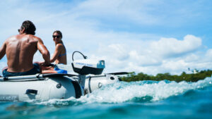 View of the back of a small inflatable boat that is being powered by an electric outboard engine while carrying two passengers.