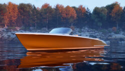 Side profile of copper-coloured open boat on a lake with trees in the background on the rocky foreshore.