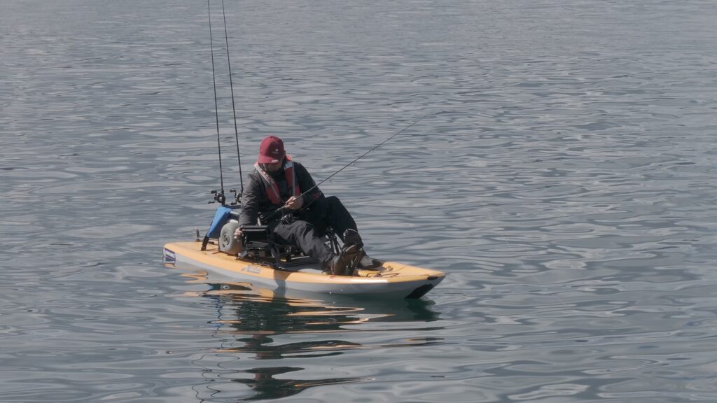 person on kayak looks at screen while holding fishing rod