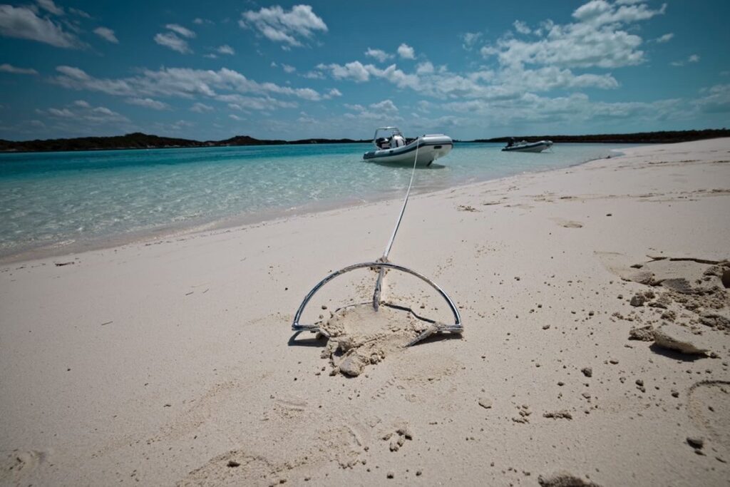 an anchor in clean sand, behind it is blue sea with dinghy