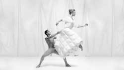 A male ballerina lifts a female dancer who is wearing a duvet as a skirt