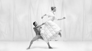 Eine männliche Ballerina hebt eine Tänzerin hoch, die eine Bettdecke als Rock trägt