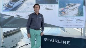 dark hair man standing by Fairline sign and stand