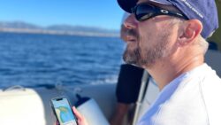 een kerel met een hoed op een boot staart naar de zee terwijl hij zijn telefoon vasthoudt waarop navigatiegegevens staan ​​van slimme navigatie
