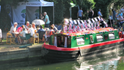canal boat decorates with UK flags docked alongside a party of people at a table. This is Ware Boat Festival cancelled due to towpath being dangerous