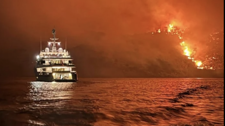 night shot with raging fire on hillside and yacht on the water in foreground