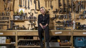 A woman sits in a workshop surrounded by tools.