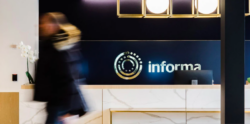 Woman walks by a desk with Informa logo in background
