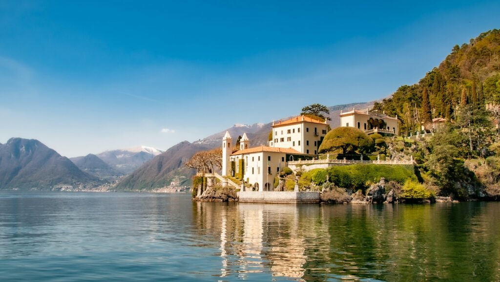 Blick auf den Comer See mit Gebäuden und Bergen im Hintergrund. Ort des tragischen Ertrinkens eines britischen Touristen, nachdem er ins Wasser gesprungen war und das Boot abgetrieben war