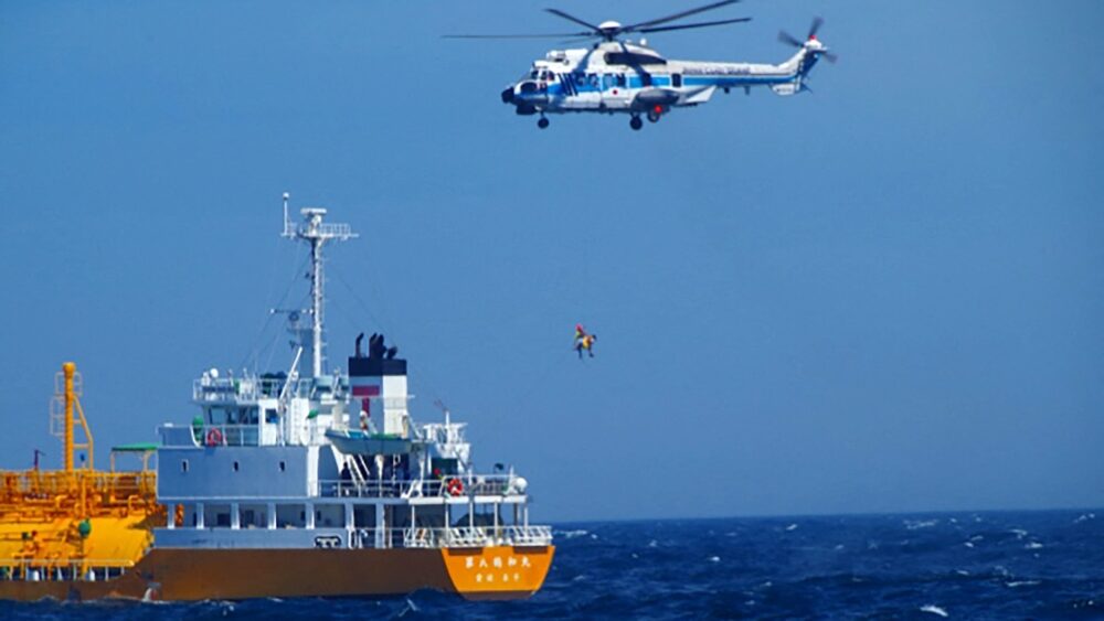 Helicopter hovers as it rescues a woman from the ocean, with a ship nearby.