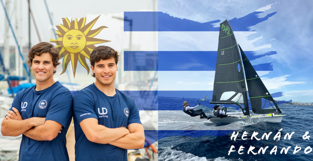 Two Olympic sailors smlle at camera next to their boat