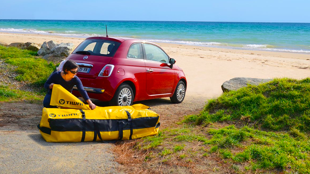 Sailor on beach packs Tiwal inflatable sailboat / dinghy into small red car