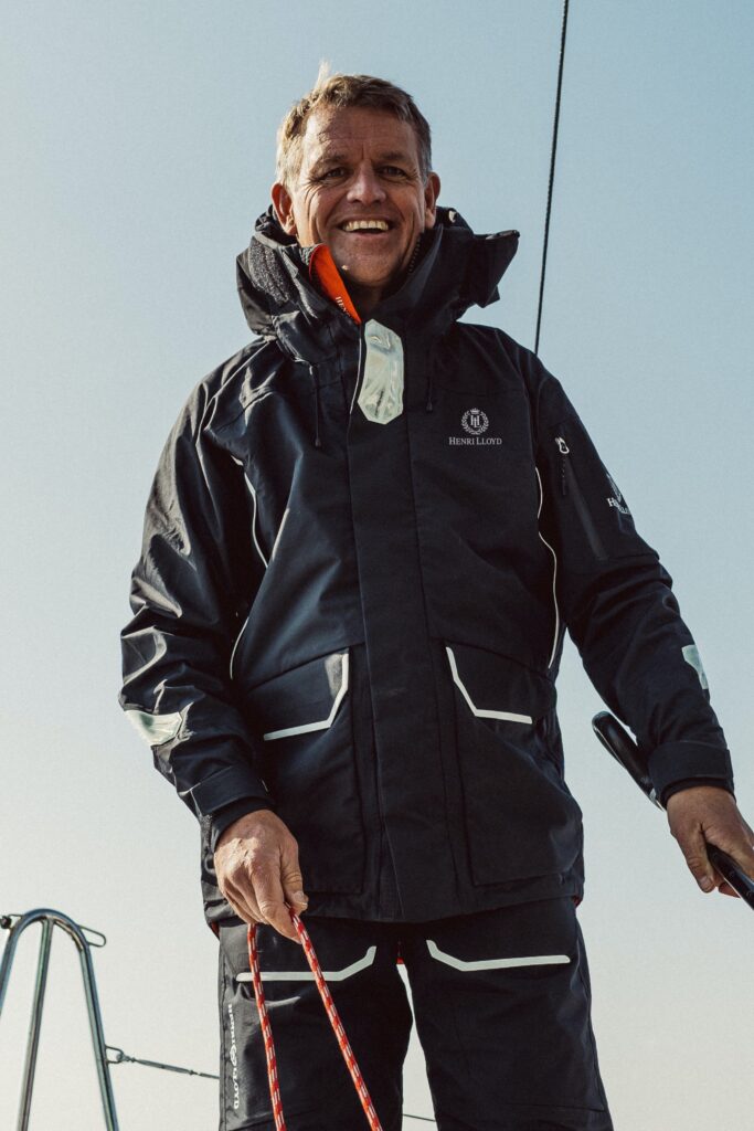 Man in black sailing gear smiles cheerily at the camera