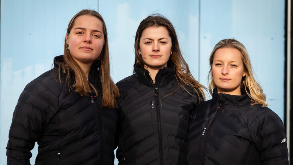 Three rowers stare at the camera. They are onshore as they prepare to row Pacific Ocean unsupported