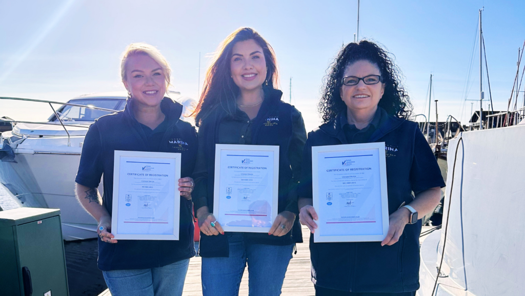 Three workers hold the accreditation certificates on a sunny day