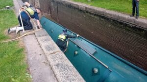 Green canal boat overturned in lock cill as workers try to rescue it from drained lock