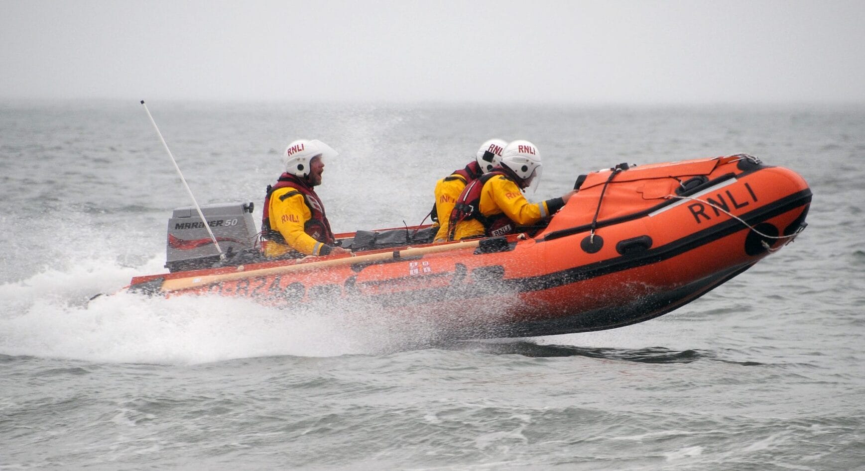 Lifeboat and lifeboat crew bracing through stormy seas on a RNLI RIB boat