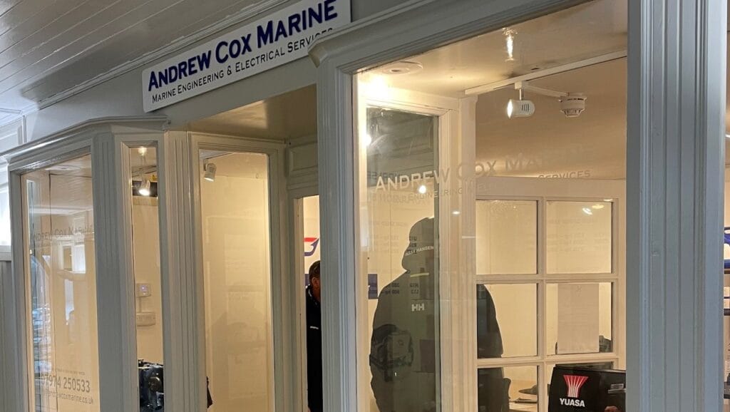A storefront with the name Andrew Cox Marine above large windows. Inside, there are visible displays of marine equipment and tools. The interior is brightly lit, and a person can be seen inside the store. marine industry news