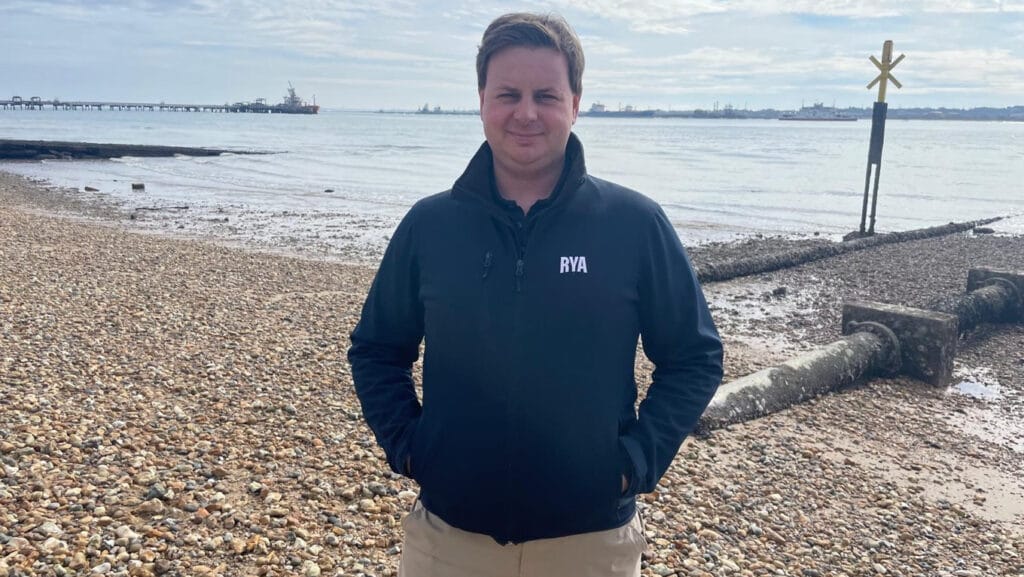 نيل ماكليود يقف على شاطئ الحصى مرتديًا سترة RYA سوداء