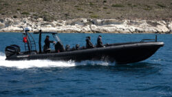 Black RIB in the water, side view, with two seated passengers and a skipper