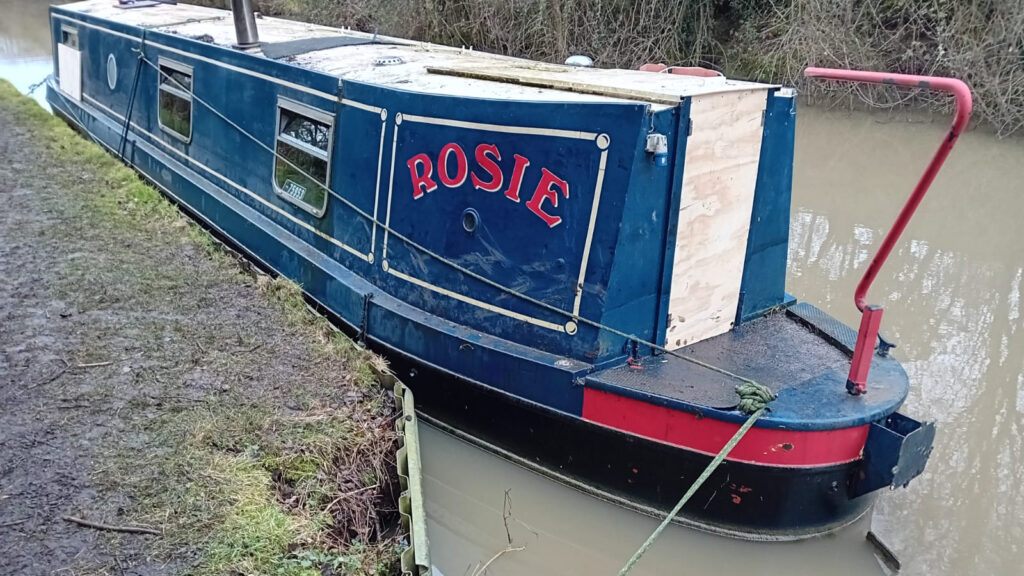 Narrowboat in water after being scuppered by thieves - boarded up back doors