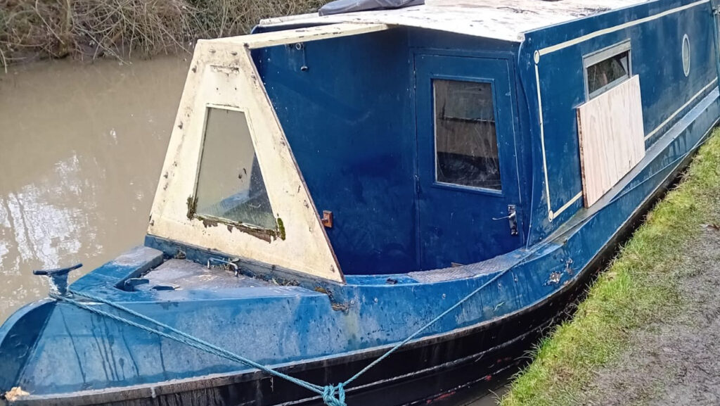 Narrowboat in water after being scuppered by thieves - wanton destruction shows boarded up access points