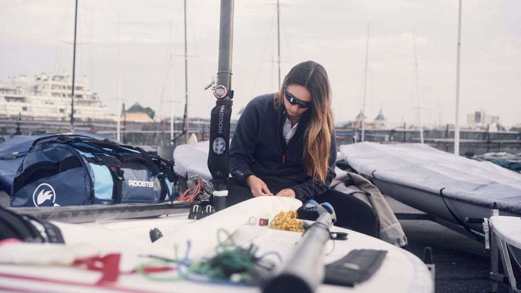 Sailor fiddles with equipment on deck of dinghy while wearing Rooster sailing gear