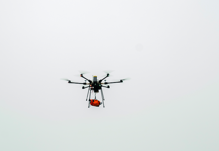 drone in flight carrying small package as shore to ship drone delivery tested