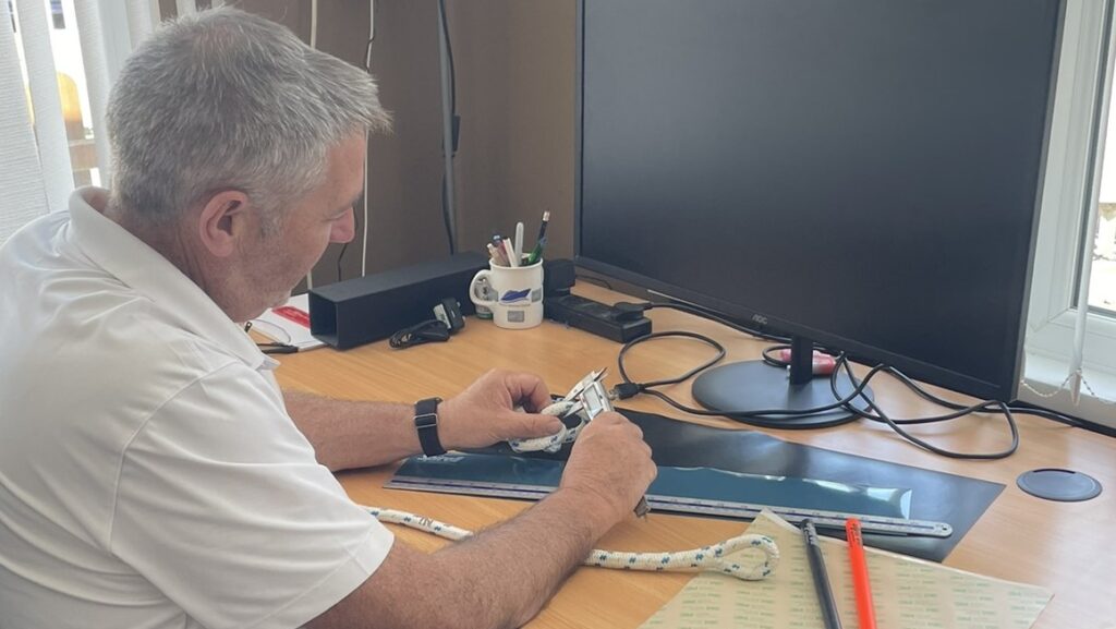 Man sits as desk in front of screen and examines Spiroll chafe guards used to stop chafing from boat ropes