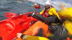 RNLI volunteers assisting a paddleboarder blown offshore