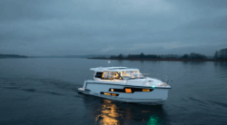 white motor boat sails toward camera with bright lights shining from windows as this is dusk