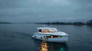 white motor boat sails toward camera with bright lights shining from windows as this is dusk