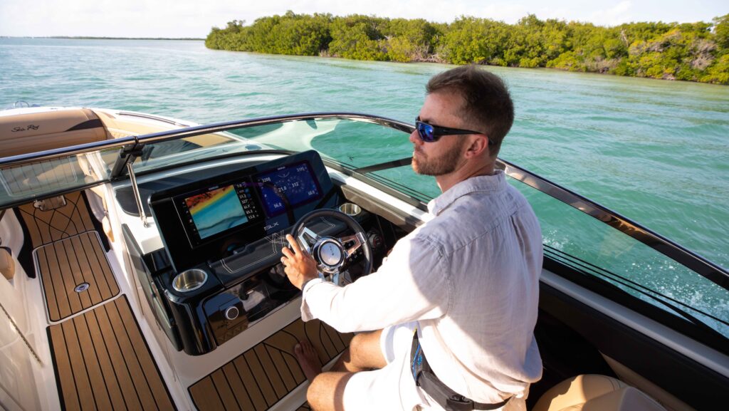 man drives a boat dressed in white shirt sitting in front of electronic console