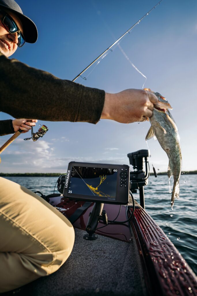 Male fisherman holds fish on boat with info console in background