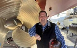man standing by boat propellor at a shipyard